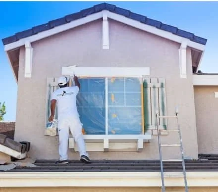 Exterior painter carefully applying paint around a protected window